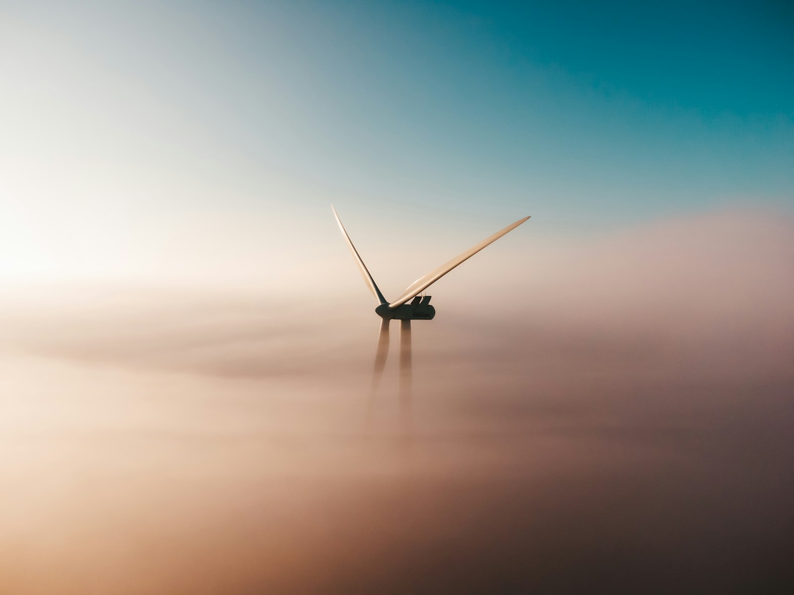A wind turbine emerging from morning fog at sunrise